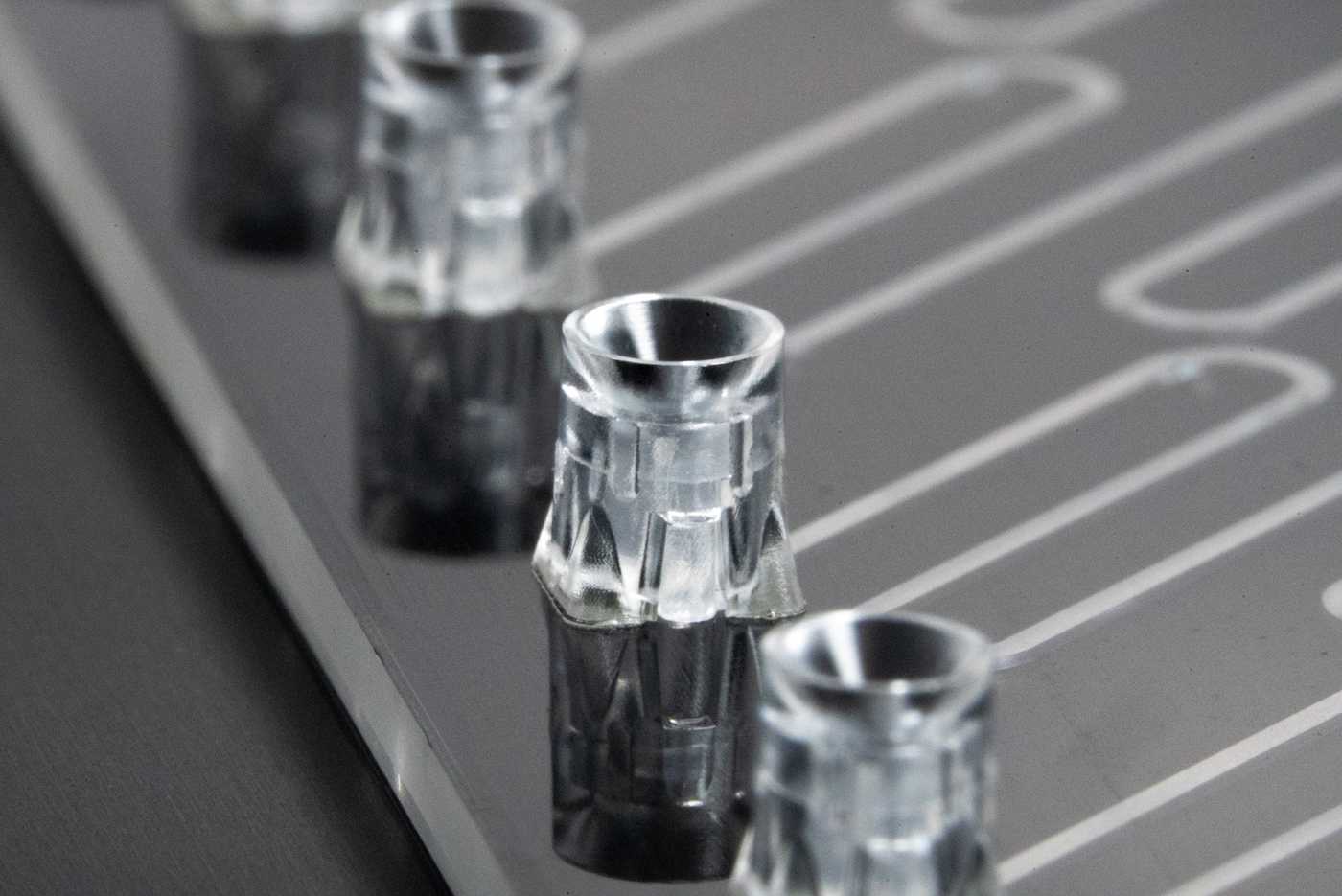 An array of pipette interfaces along the edge of a microfluidic device. Each pipette interface is connected to a meandering fluidic channel.