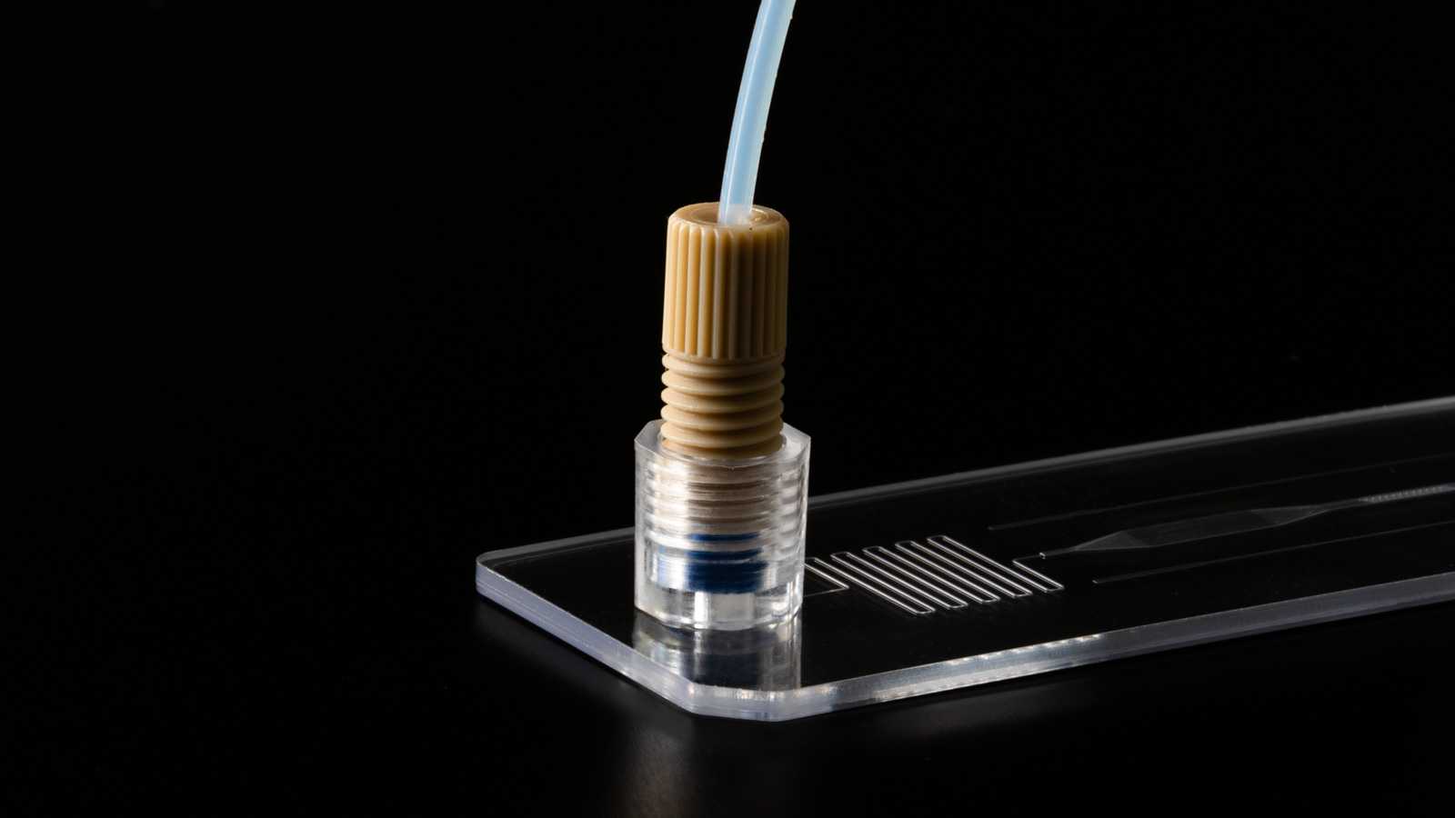 A slide format microfluidic device with a 1/4-28 port connected to tubing using a nut.